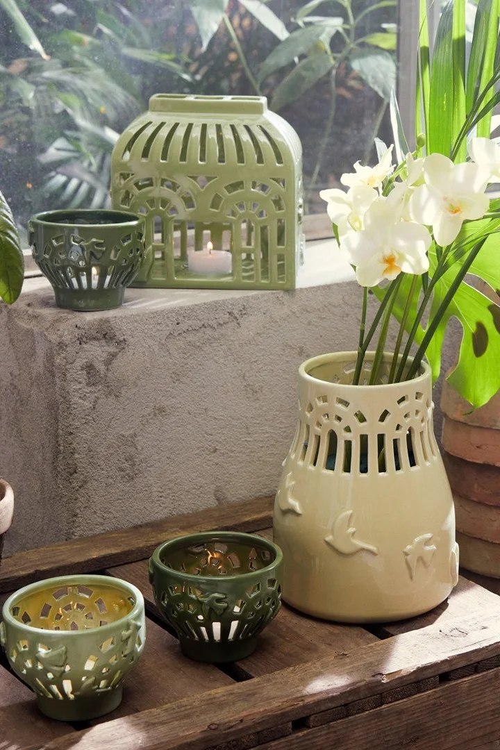 Die Windlichter und Vase aus der Orangery-Kollektion von Kähler in verschiedenen Grüntönen stehen draußen auf einer Bank und verleihen jedem Außenbereich den perfekten Boho-Stil.