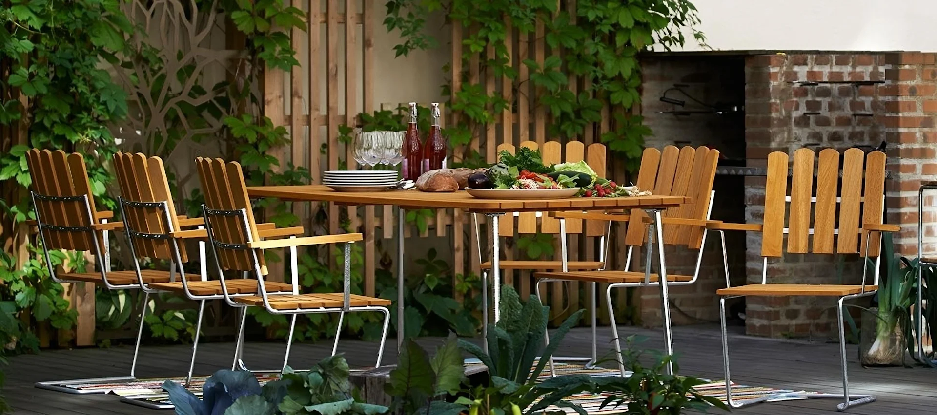 Eine Marke, die für die Gartenmöbel-Trends 2025 wichtig ist: Grythyttan. Hier ist die Klassiker-Serie, bestehend aus einem großen Tisch und Stühlen auf einer Terrasse zu sehen.