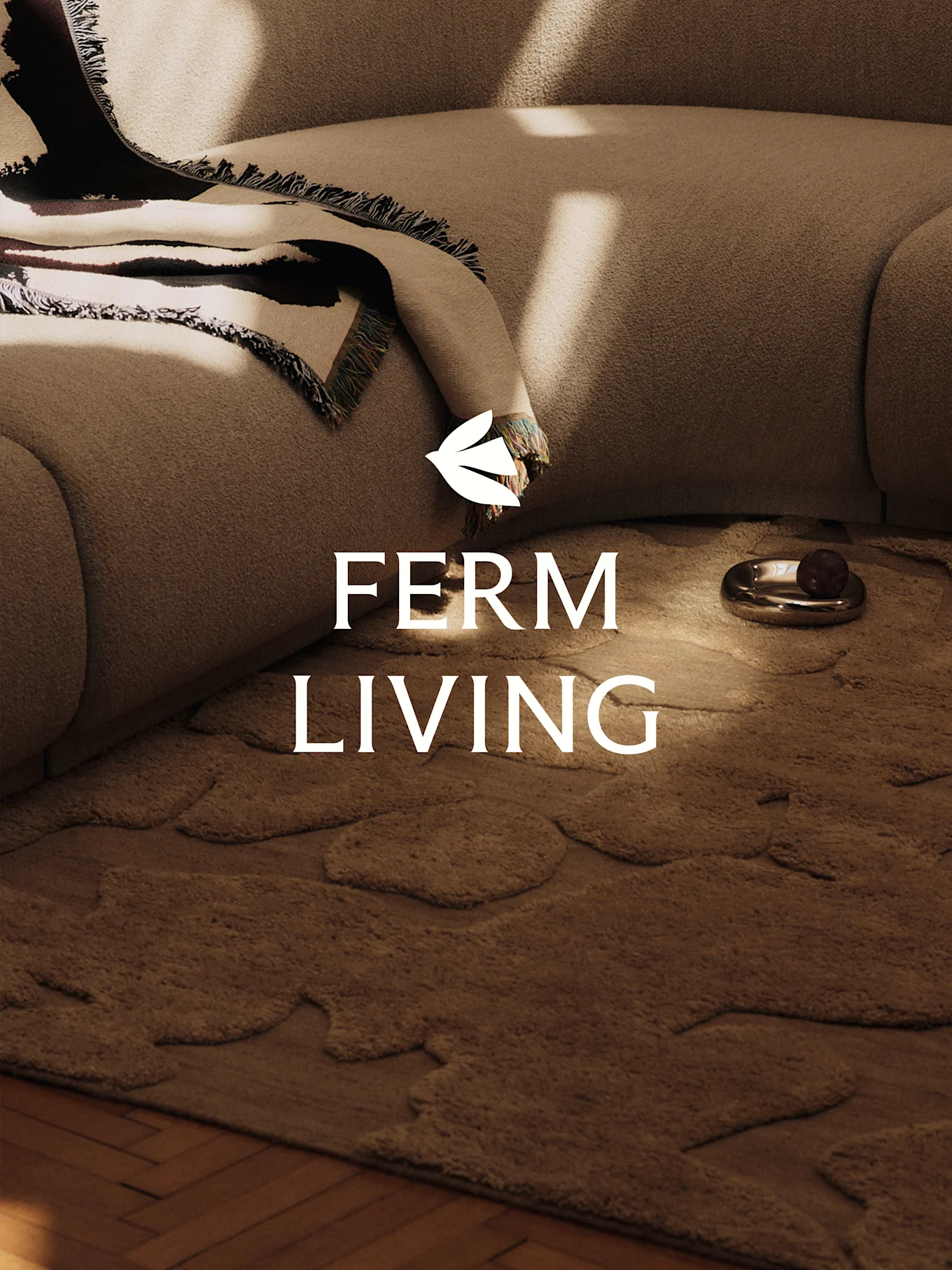 Eine gemütliche Szene mit einem hellbraunen strukturierten Sofa, einer gemusterten Decke, einem braunen Teppich mit organischen Formen und einer dekorativen Schale.