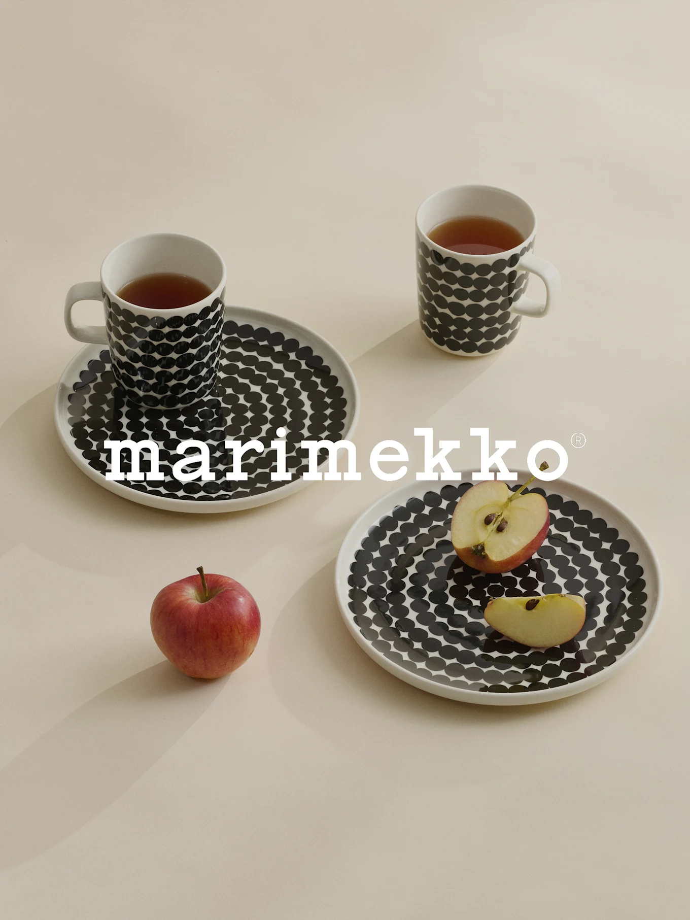 Zwei Tassen und Teller mit schwarzen Punkten, Tee, roter Apfel, Marimekko-Logo.