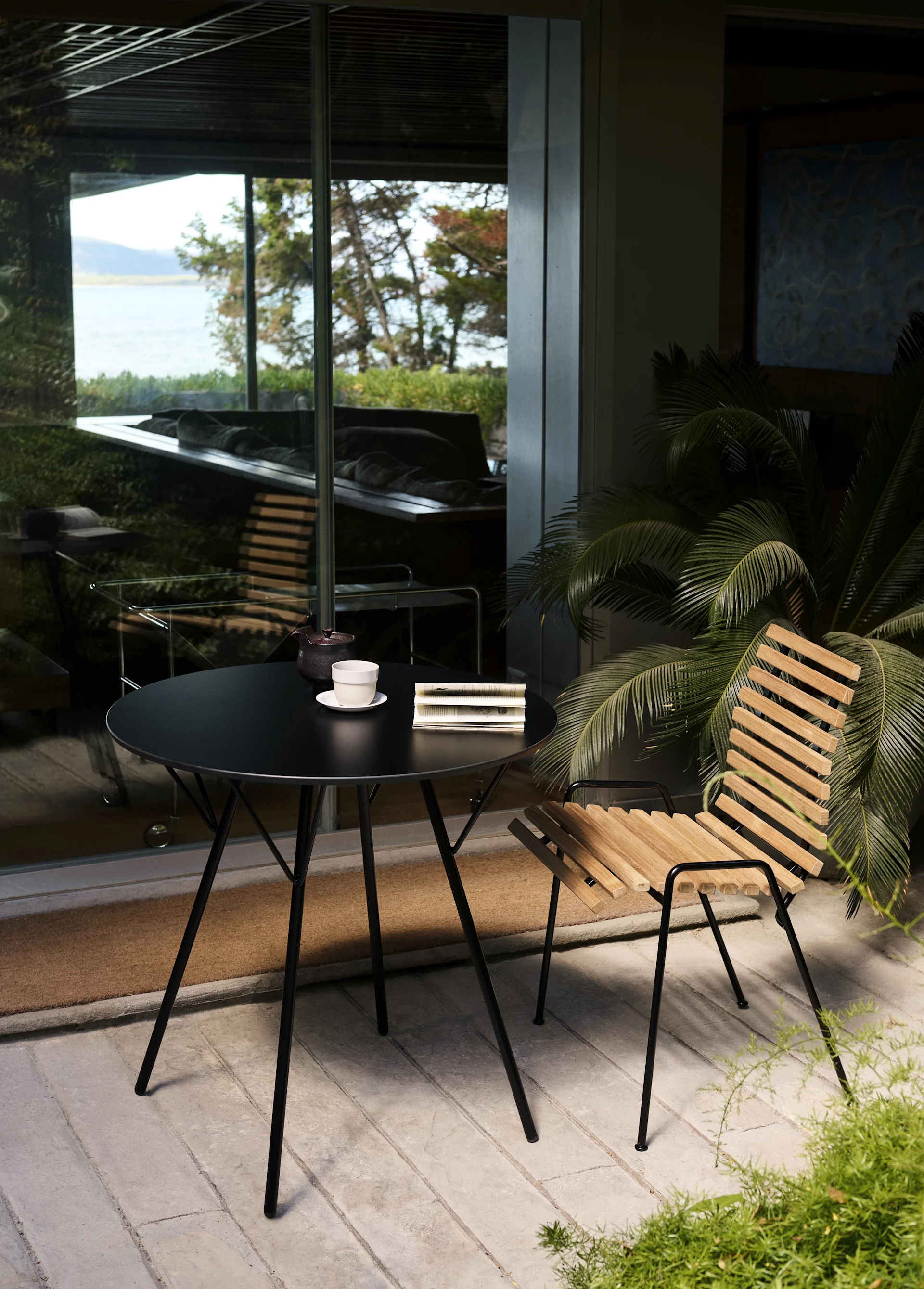 Der RFH RD4 Terrassen-Seitenstuhl von &Tradition steht mit einem runden Tisch auf einer Terrasse.
