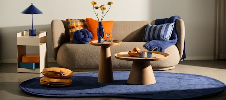 Die Wohntrends für den Herbst 2023 sind bunt und gewagt! Hier sehen Sie blaue Details wie einen Teppich und eine Lampe in einem neutral gehaltenen Wohnzimmer.