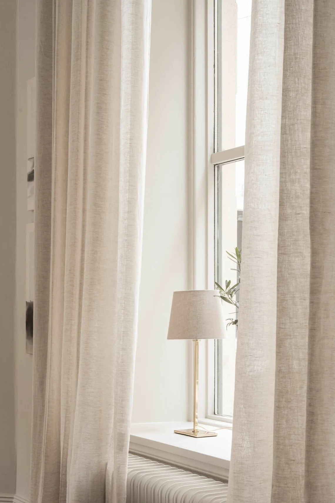 Eine Tischleuchte von Watt & Veke steht auf einem Fensterbrett, umgeben von hellen Gardinen.