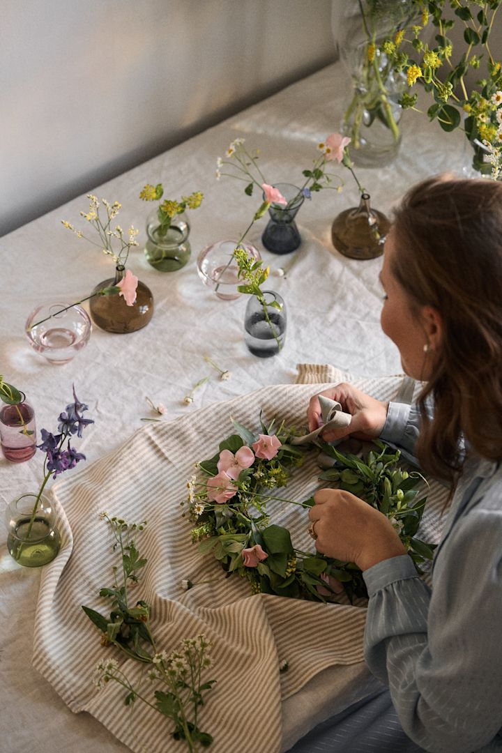 Eine Frau sitzt an einem Tisch und bastelt fürs Midsommarfest in Schweden einen Blumenkranz.