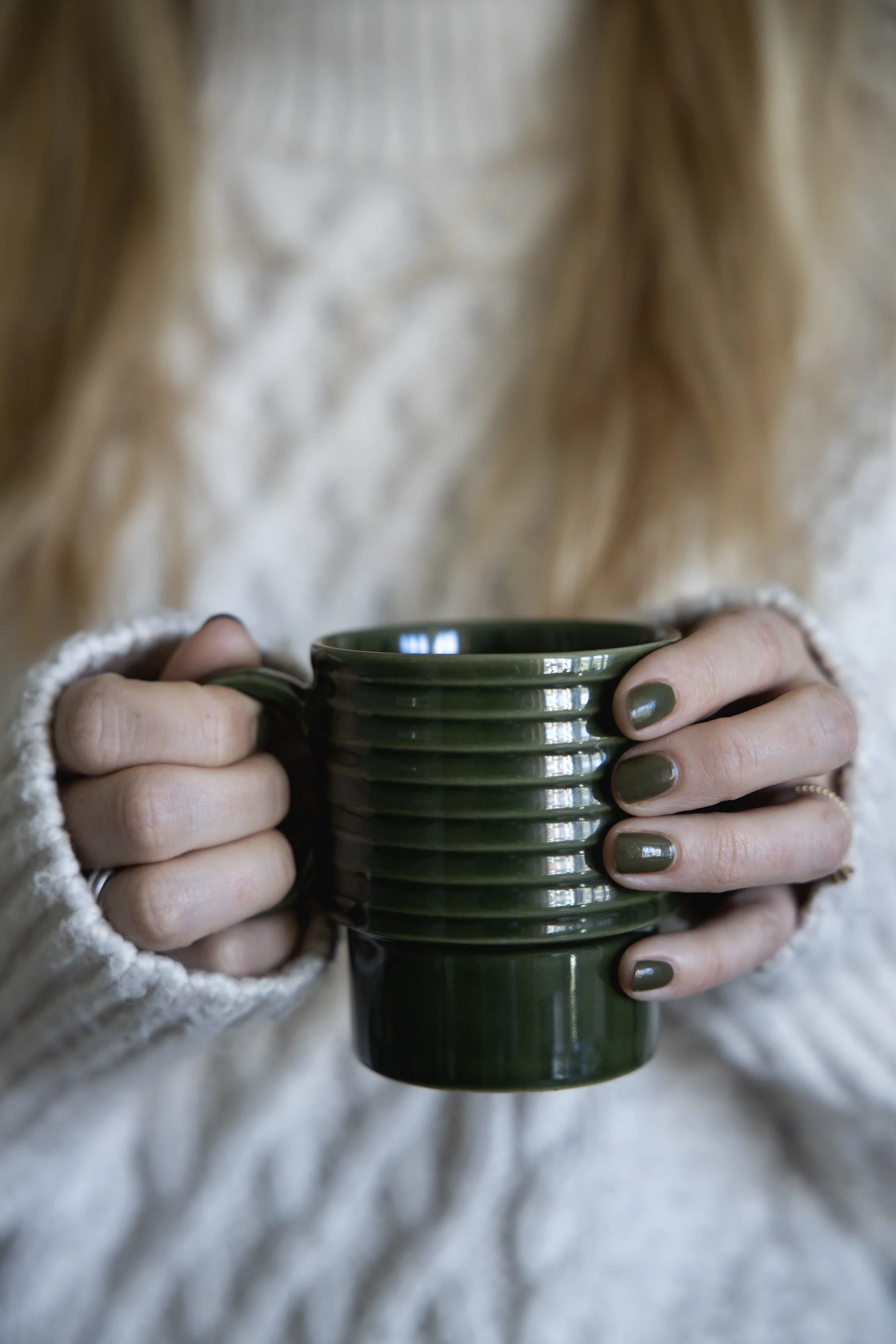 Eine Frau in weißem Pullover hält eine grüne Tasse aus der Coffee & more-Kollektion von Sagaform in den Händen.