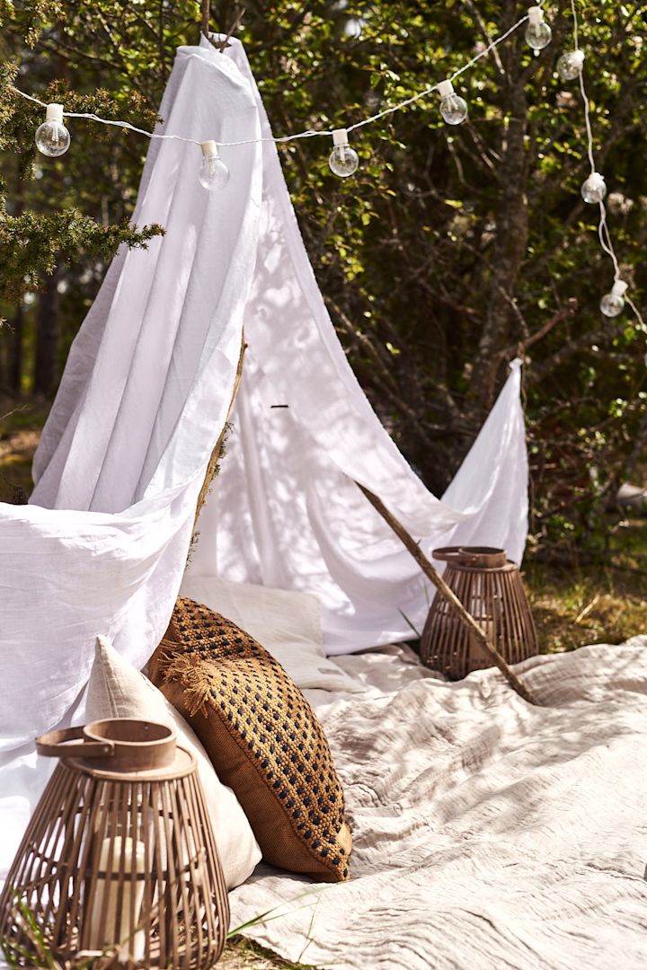 Glamping mit einem kleinen Zelt zu Hause im Garten mit vielen Kissen und Laternen.