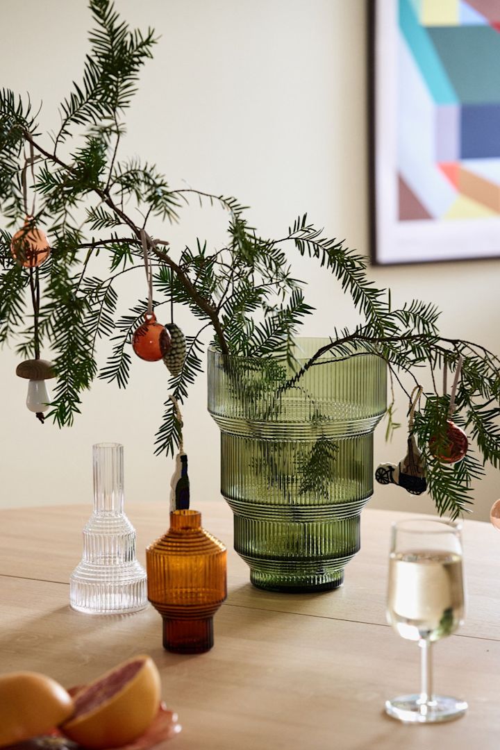 Weihnachtsdekoration basteln mit Tannengrün: Hier sehen Sie Tannenzweige in der grünen Pavillon Vase von Kosta Boda, dekoriert mit Weihnachtskugeln auf einem Tisch stehen.