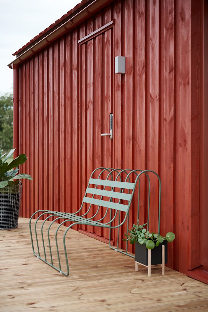 Gartenmöbel-Trends 2025: Das Gardeners Sofa von Design House Stockholm in Grün steht auf einer Terrasse vor einem roten schwedischen Holzhaus.