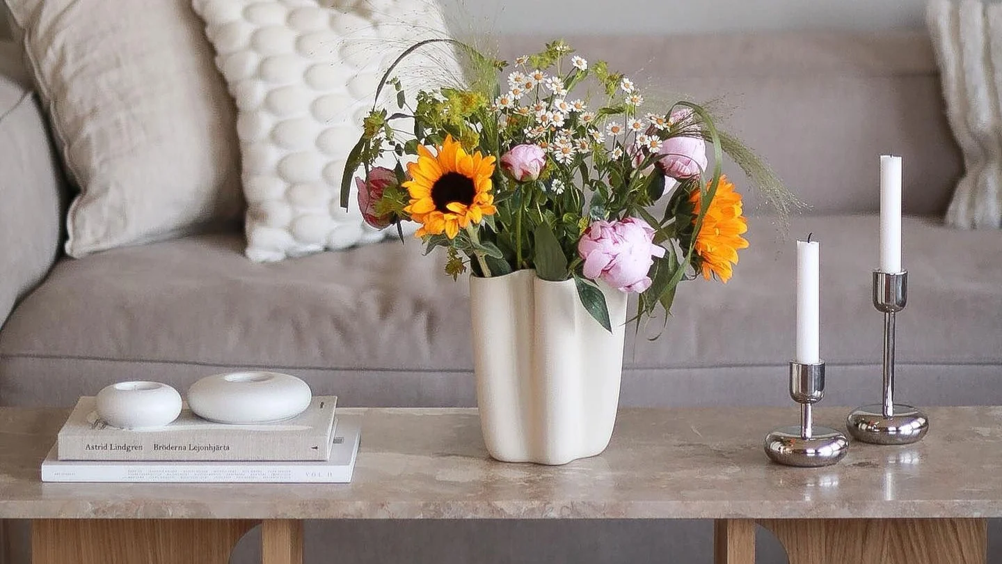 Der Androgyne Loungetisch von Audo Copenhagen ist dekoriert mit frischen Blumen, zwei Nappula Kerzenhaltern von Iittala und den Stone Windlichtern von Scandi Living.