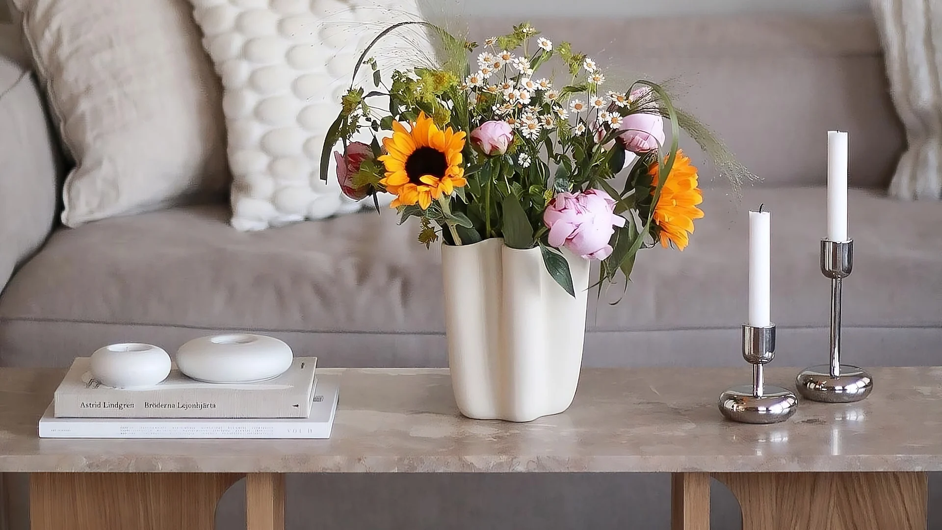 Der Androgyne Loungetisch von Audo Copenhagen ist dekoriert mit frischen Blumen, zwei Nappula Kerzenhaltern von Iittala und den Stone Windlichtern von Scandi Living.