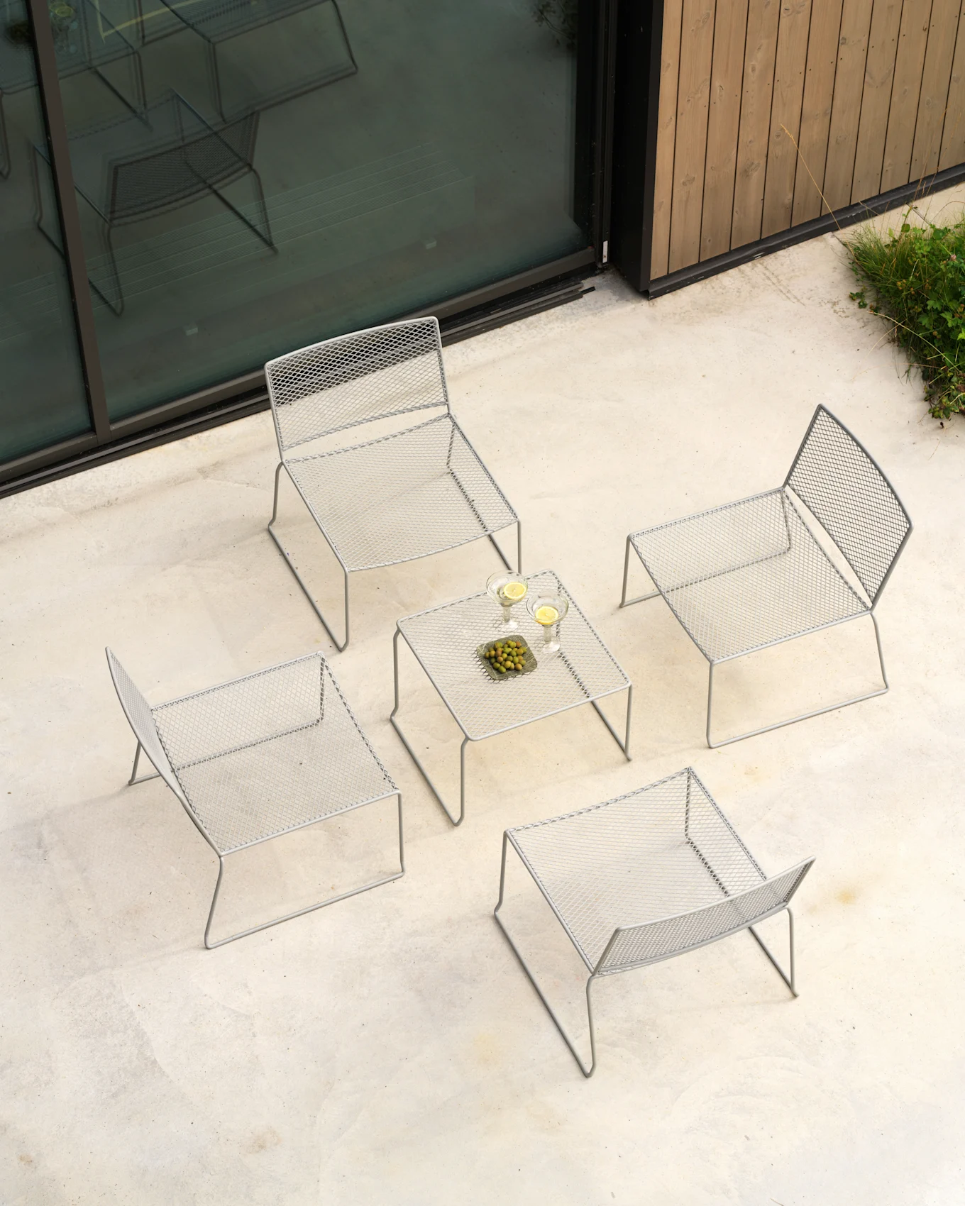 Draufsicht auf eine hellgraue Outdoor-Loungegruppe: vier Netzstühle, ein Tisch mit Getränken und Oliven auf Beton.