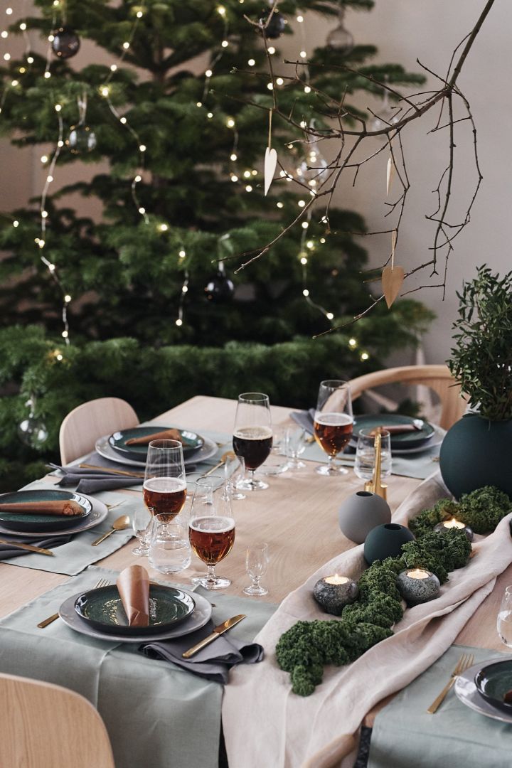 Der Tisch ist für das Weihnachtsessen mit einer grünen Dekoration mit grünen Tellern, goldenem Besteck und grünen Vasen hergerichtet. 