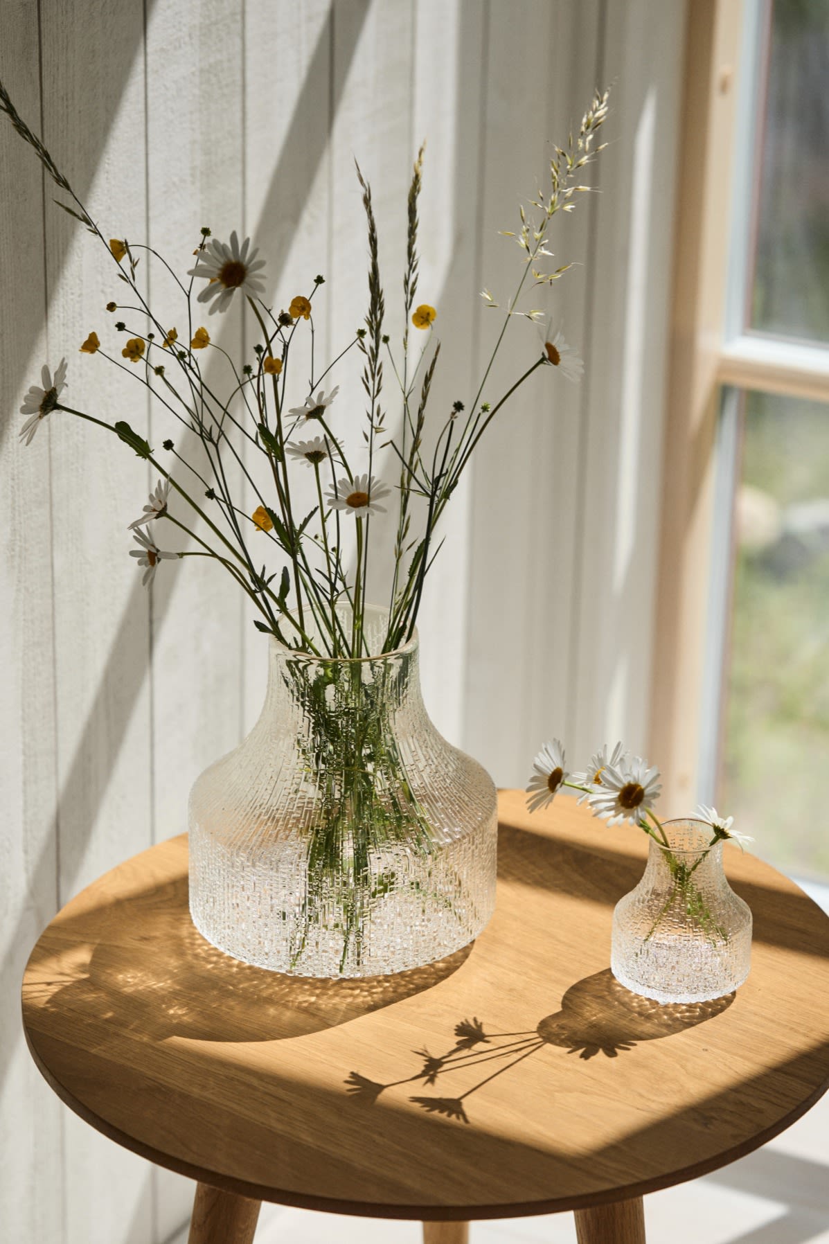 Die beste Vase für kleine Sträuße und einzelne Blumen ist eine kleine oder eine Mini-Vase wie die Ultima Thule-Vasen, die Sie hier im Sonnenschein auf einem Tisch sehen. 