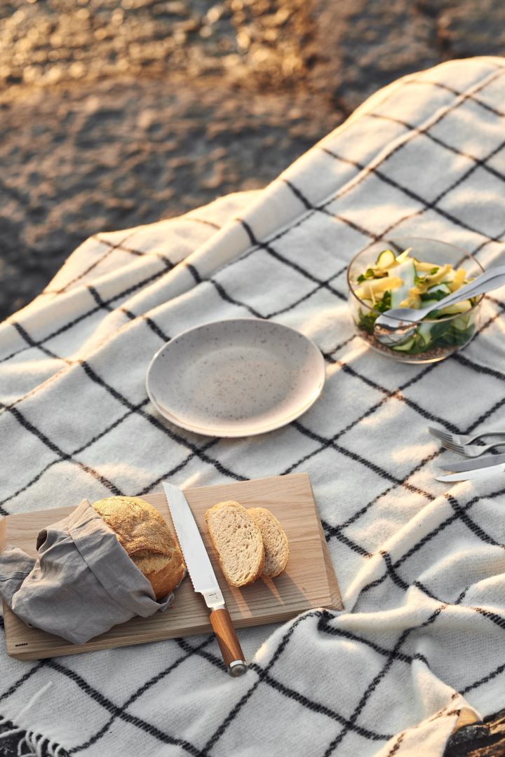 Bringen Sie die Wolldecke von Klippan Yllefabrik zu Ihrem Sommerpicknick mit, auf dem Sie sitzen und einen leckeren Sommersalat und ein Sandwich genießen können.