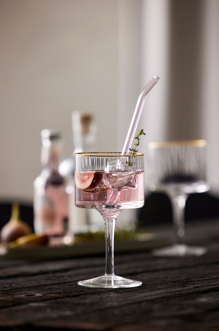 Ein lilafarbener alkoholfreier Cocktail mit Glasstrohholm und dekoriert mit Thymian steht auf einem Tisch, serviert im Palermo Gold Gin & Tonic Glas von Lyngby Glas.