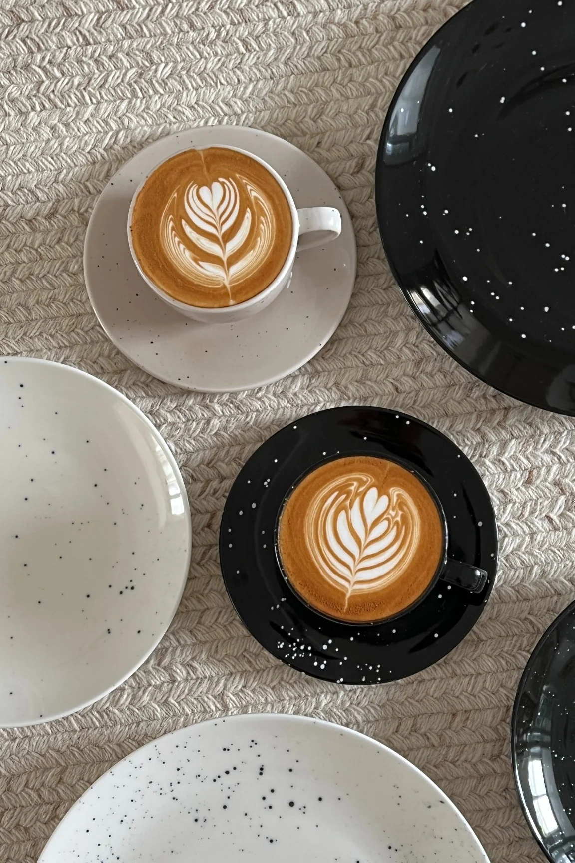 Zwei Tassen mit kunstvoll angerichtetem Kaffee in Schwarz und Beige aus der Freckle-Kollektion von Scandi Living umgeben von Tellern im Zuhause von @Avery-P.