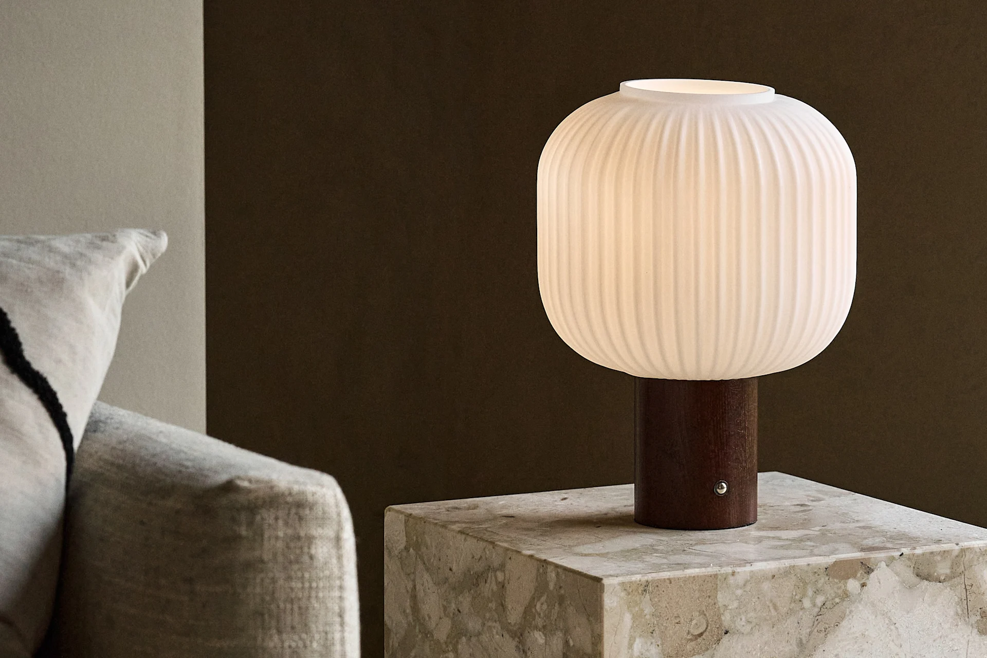 Weiße gerippte Tischlampe mit Holzfuß auf einem Marmorbeistelltisch neben einem Sofa.