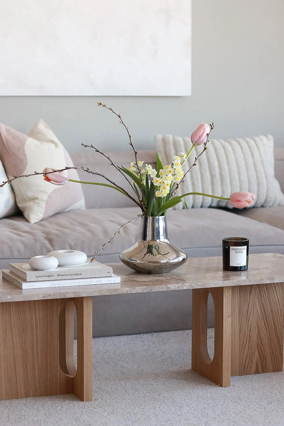 Ein frühlingshaft dekorierter Couchtisch von @picsbyellen: Auf dem Androgyne Loungetisch von Audo Copenhagen steht die chromfarbene Henning Koppel Vase von Georg Jensen mit Tulpen darin, daneben Kerzen und Kerzenhalter.