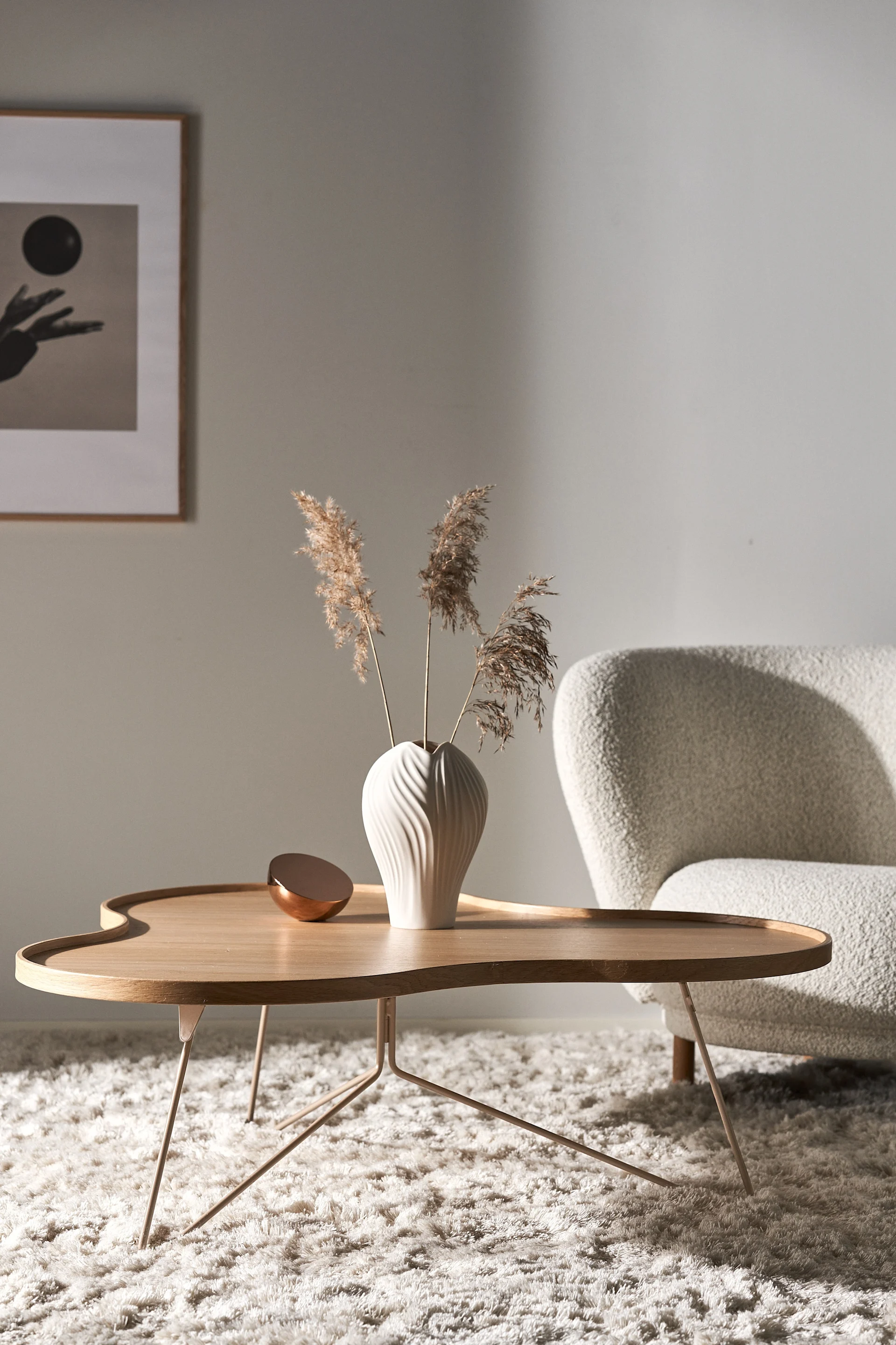 Der helle Flower mono Tisch von Swedese steht in einem beigefarbenem Wohnzimmer mit beigefarbener Couch und beigefarbenem Teppich. Auf dem Tisch steht die Anna Vase mit Trockenblumen, ebenfalls von Swedese.