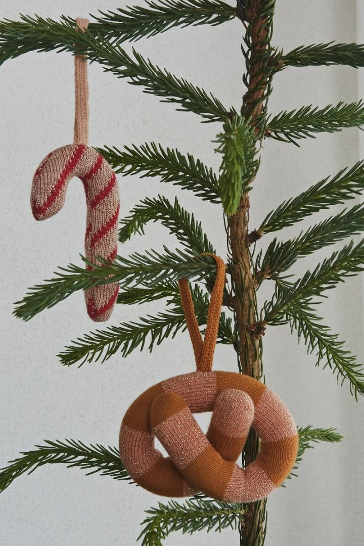 Angesagte skandinavische Weihnachtsdekoration – gestrickte Zuckerstangen und Bretzeln von OyOy hängen in einem Weihnachtsbaum. 