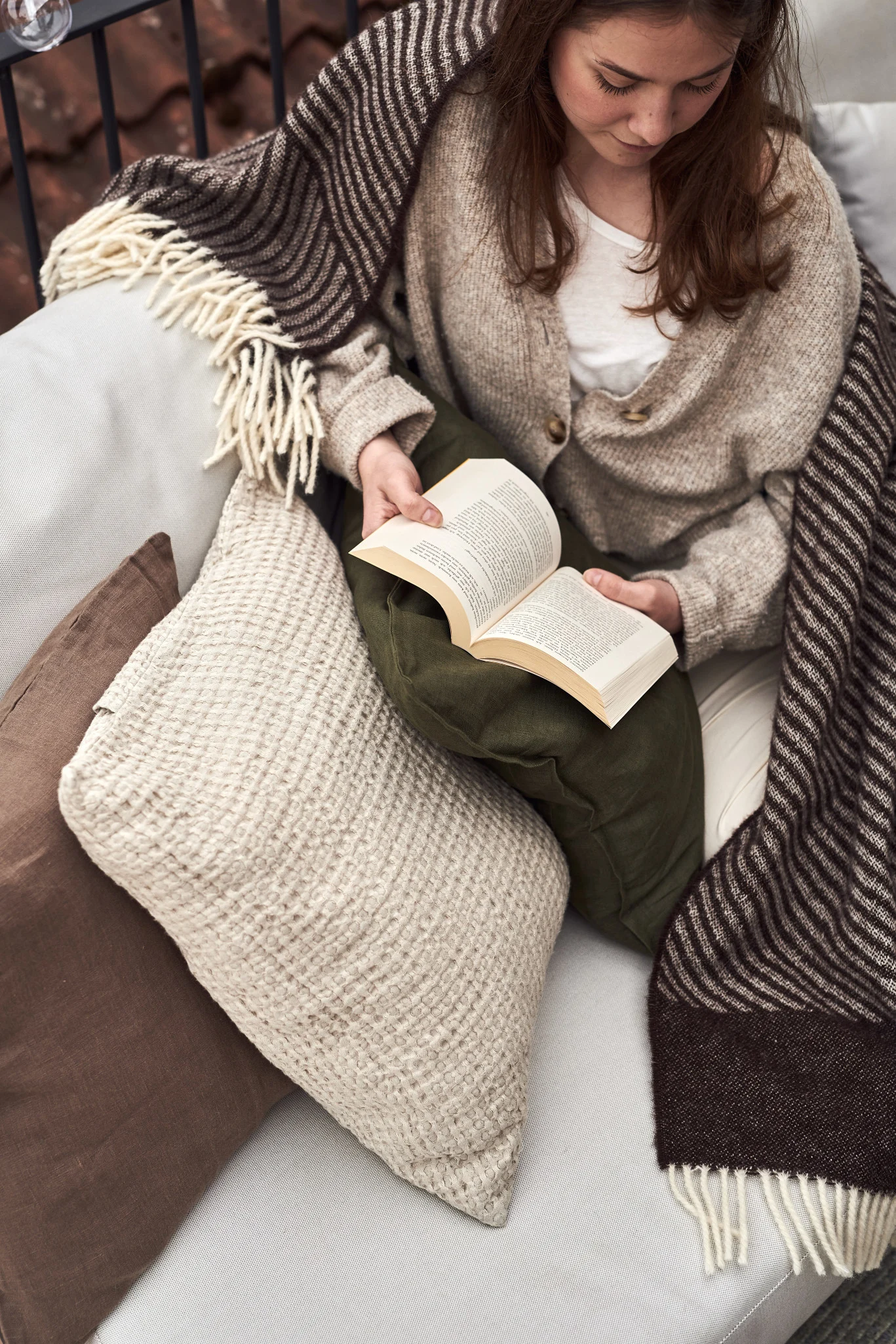 Eine Frau sitzt auf einem Sofa auf dem Balkon und liest ein Buch.