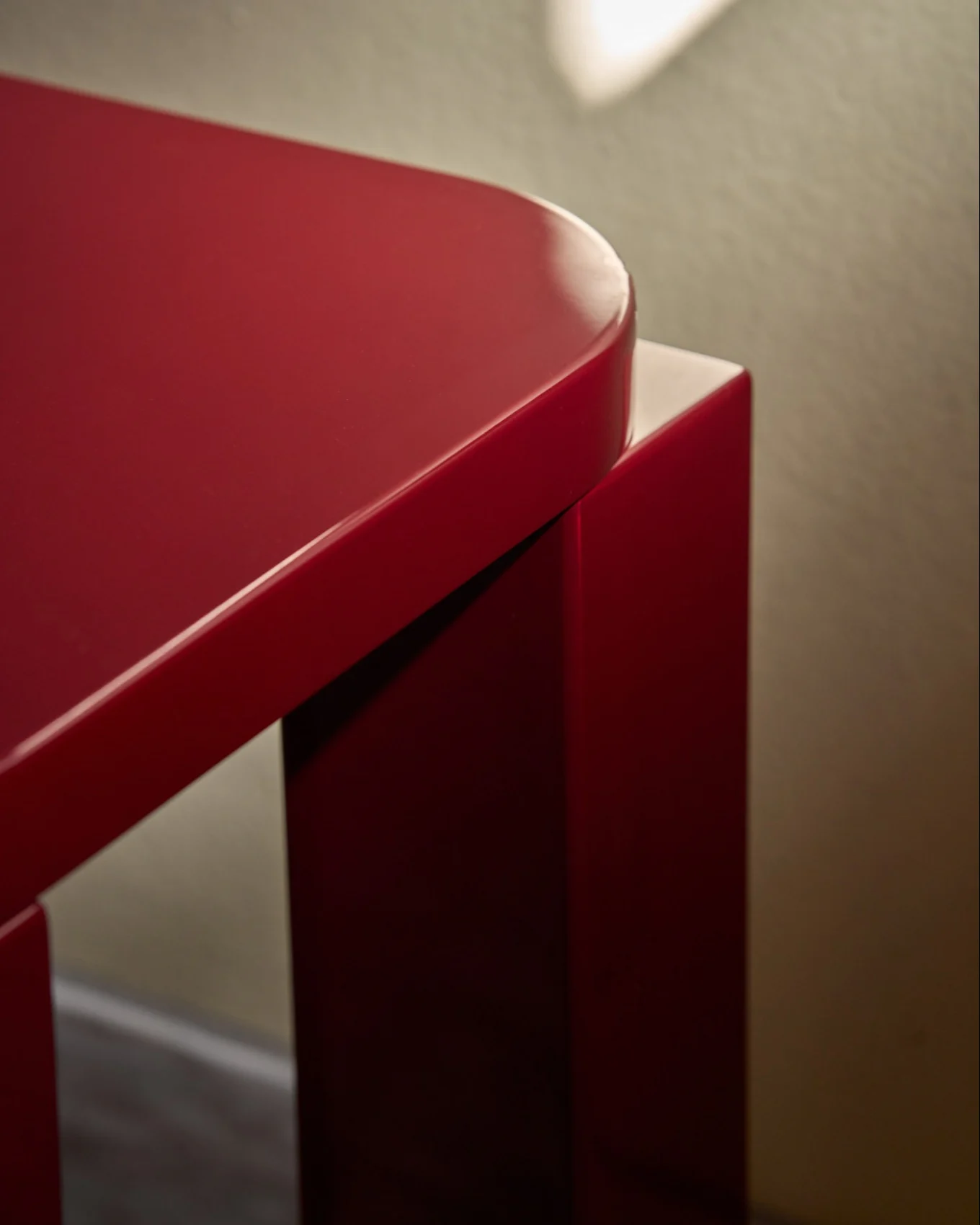 Ein glänzender roter Hocker mit abgerundeter rechteckiger Platte auf einem gefliesten Boden neben einer Wand mit roten Fliesen.