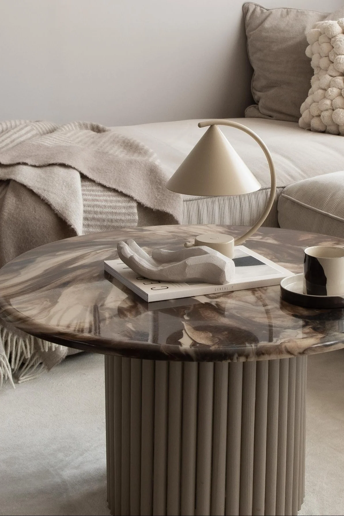 Ein Couchtisch mir Marmor-Tischplatte ist dekoriert mit einer Kaffeetasse, einer skulpturalen Hand und der Meridian Tischleuchte von Ferm Living.