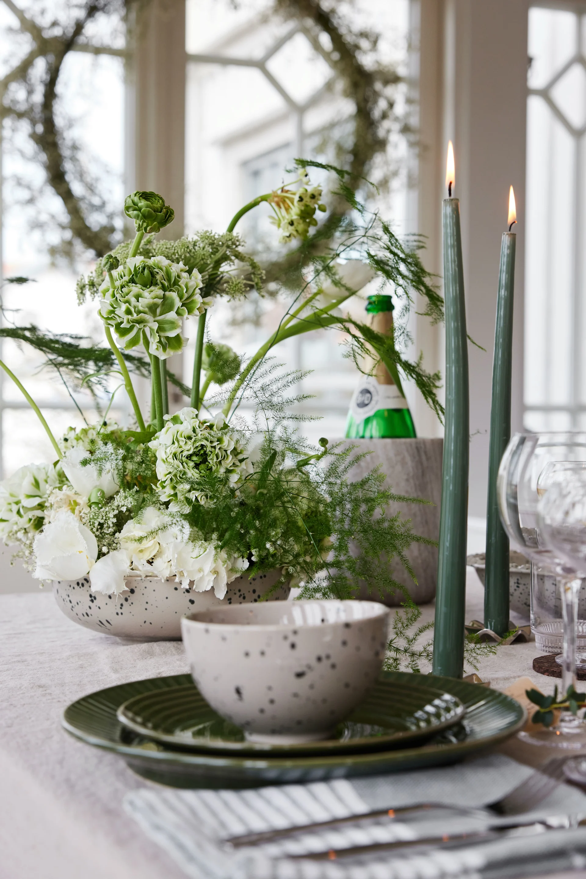 Ein gedeckter Tisch mit Tellern, Blumen, Kerzen und einem Weinkühler.