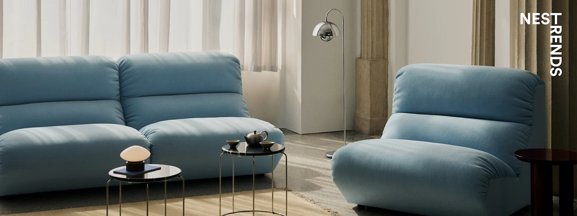Modernes Wohnzimmer mit zwei hellblauen Sofas, schwarzen Marmor-Beistelltischen und eleganten Lampen.