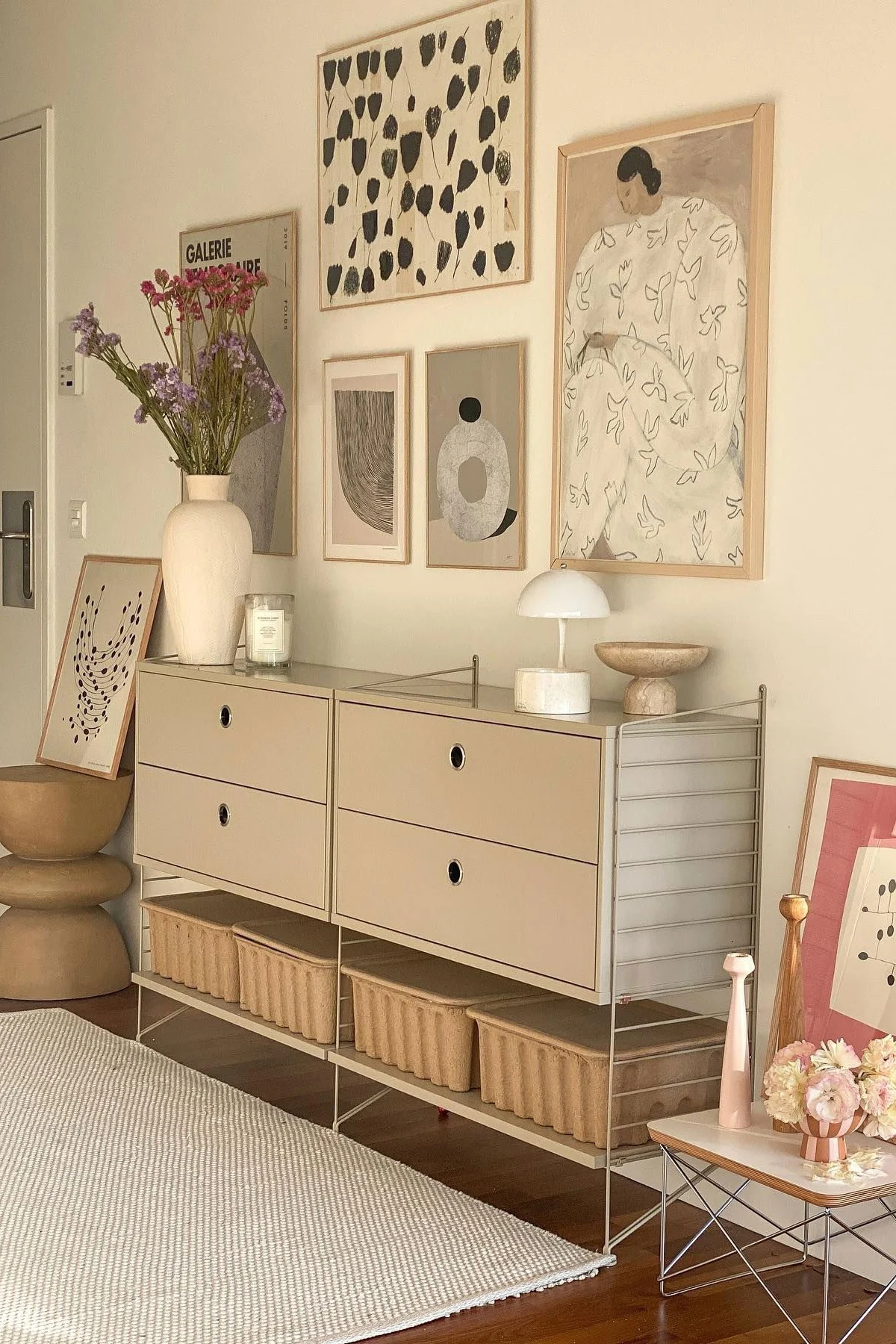 Ein modernes Zimmer mit einem beigefarbenen modularen Schrank, Schubladen und Aufbewahrungskörben. Eine Blumenvase, Lampe und abstrakte Kunst schmücken den Raum.