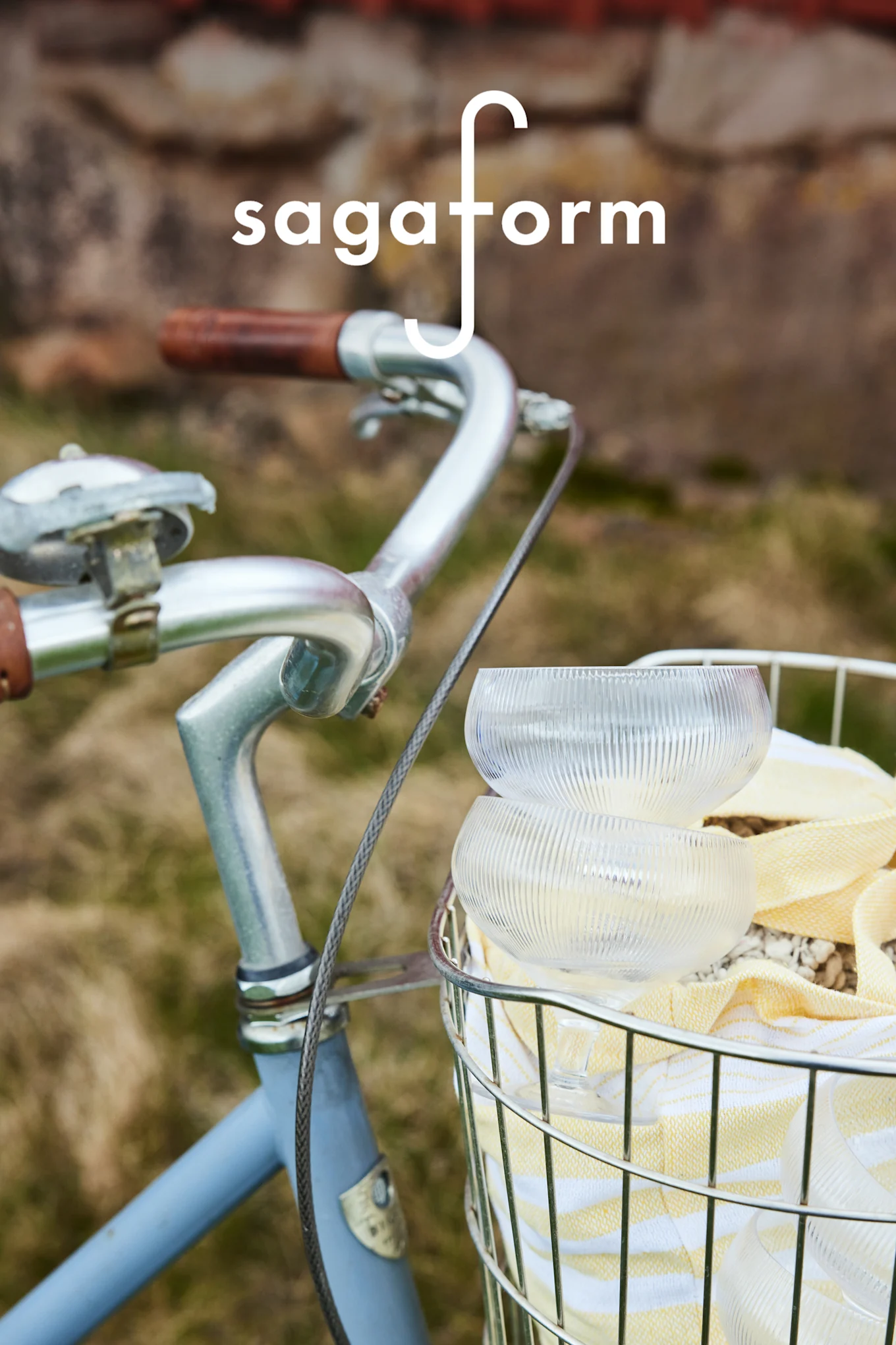 Zwei klare, gerippte Glasschalen und ein gelb gestreiftes Handtuch in einem Fahrradkorb. 'sagaform'-Logo.