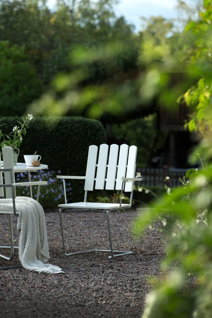 Grythyttan Reportage: Hier sehen Sie einen weißen Gartenstuhl aus Holz an einem Tisch im Grünen stehen.