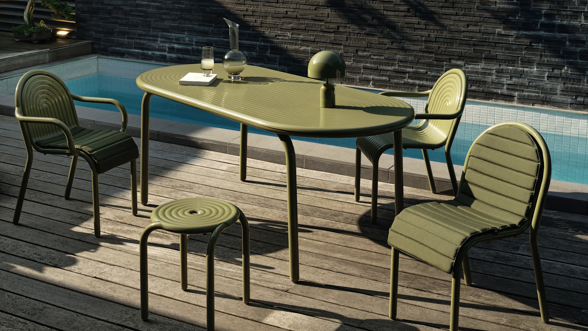 Gedämpft grünes Outdoor-Essset mit ovalem Tisch, drei gepolsterten Stühlen und einem Hocker auf Holzdeck am Pool. Eine Lampe, Karaffe und ein Glas stehen auf dem Tisch.