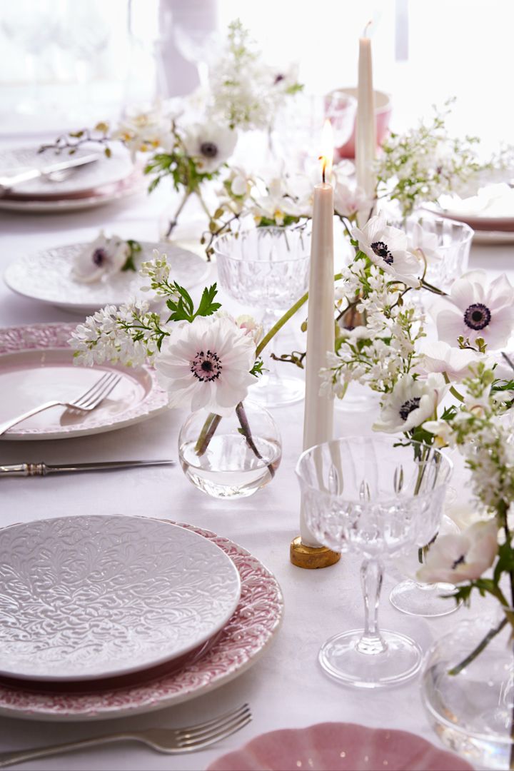 Eine Tischdekoration in Weiß und Rosa, die Teller stammen aus der Lace-Kollektion von Mateus, dazu stilvolle Gläser, Kerzen und Blumen.