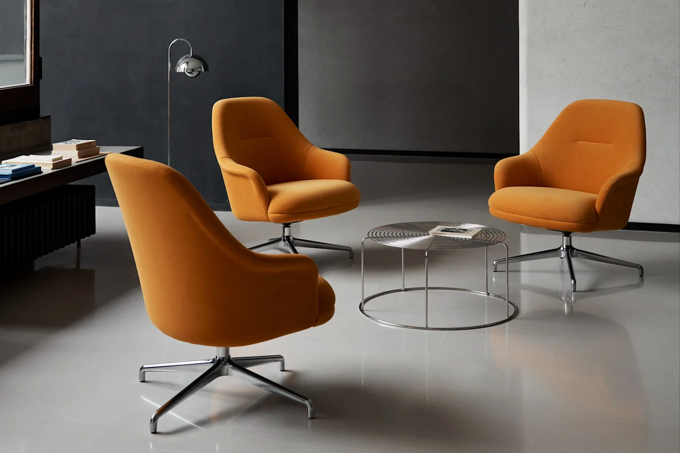 Drei orangefarbene Drehsessel, die um einen runden Couchtisch aus Chrom in einem modernen Raum angeordnet sind.
