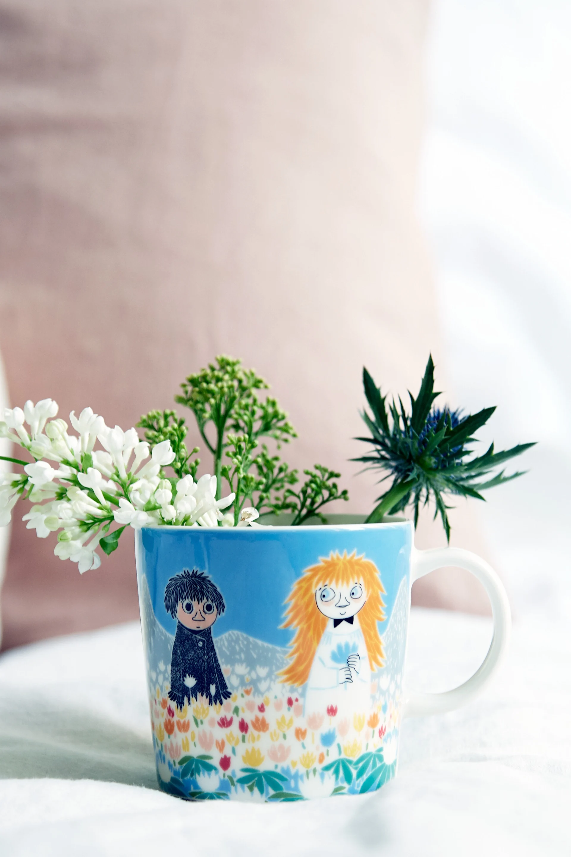 Die Mumin-Tasse "Freundschaft" steht auf einem Tisch, darin befinden sich Blumen.