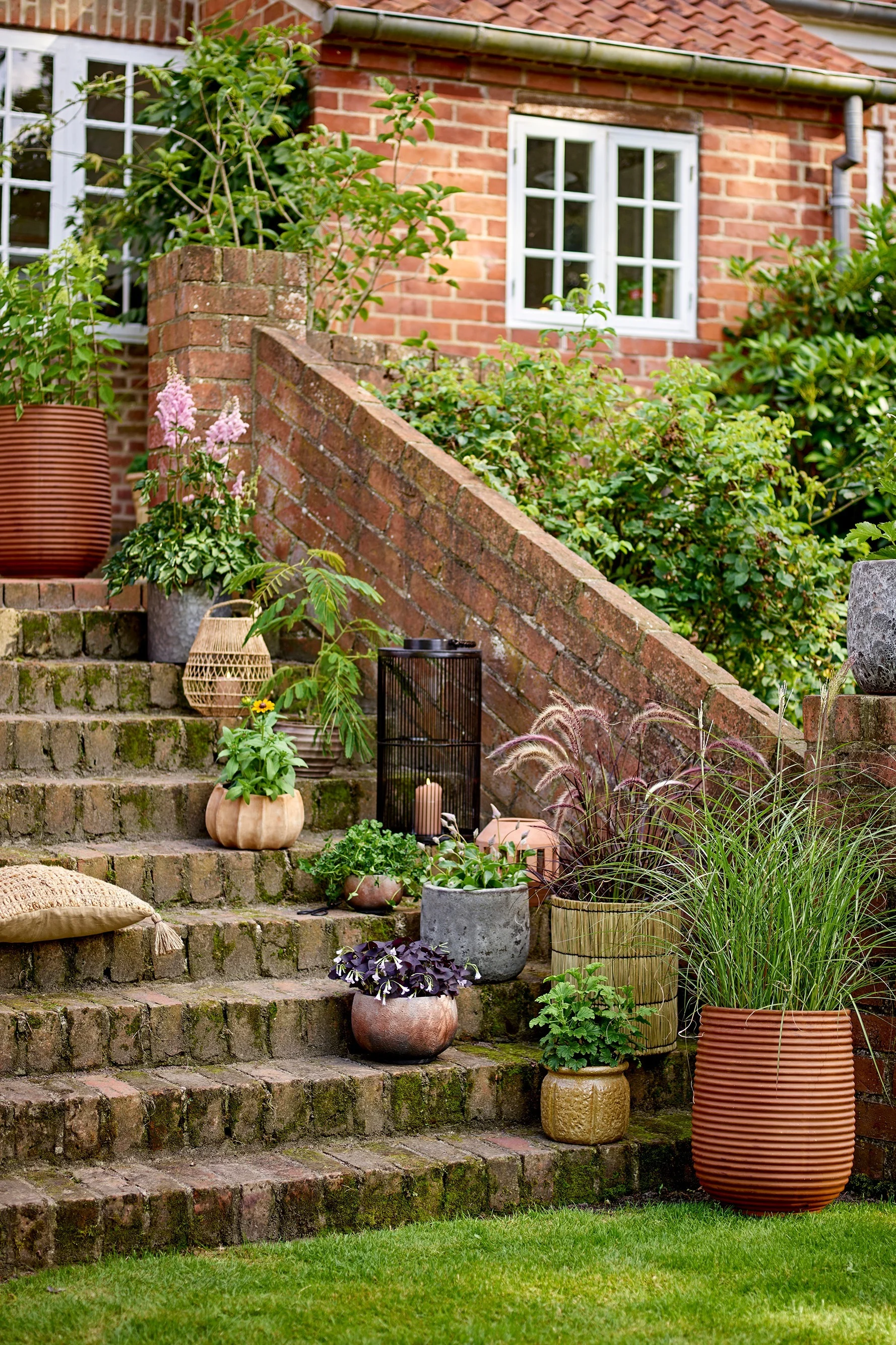 Auf einer Treppe im Garten stehen verschiedene Blumentöpfe im Boho-Stil mit Pflanzen darin, darunter der Mesola Blumentopf von Bloomingville.