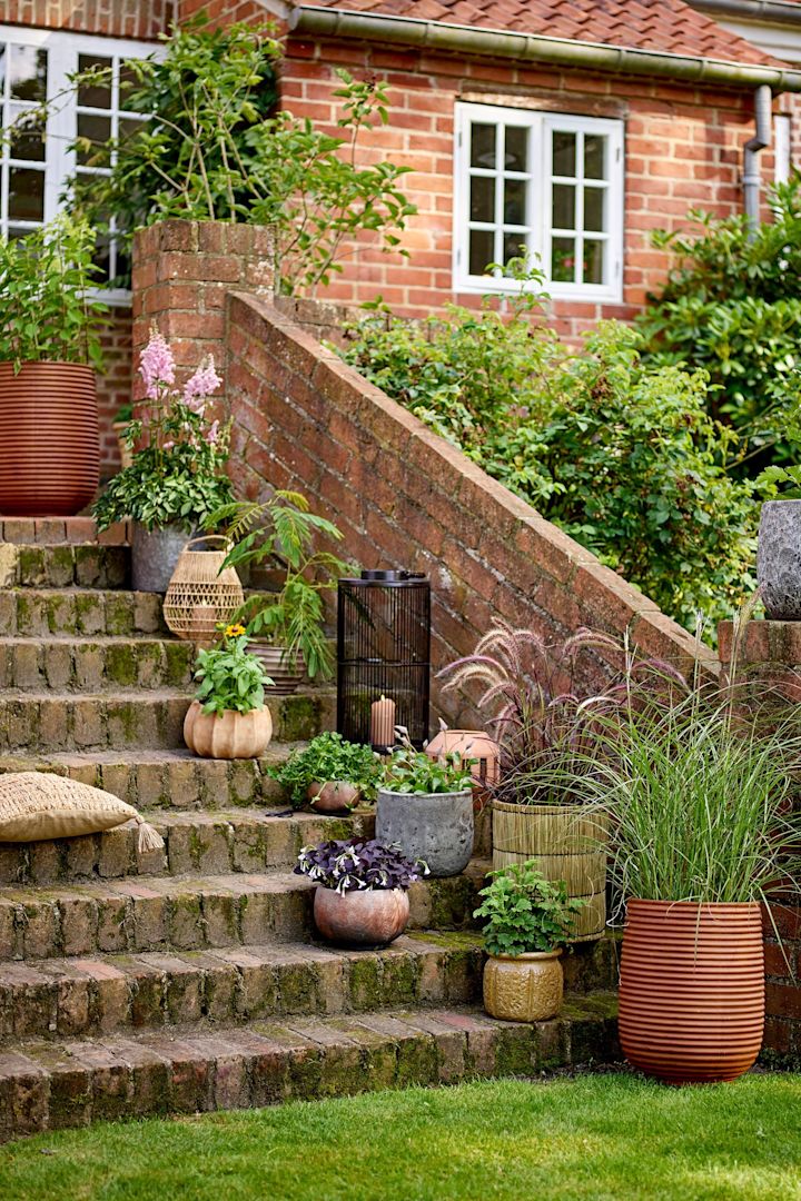 Auf einer Treppe im Garten stehen verschiedene Blumentöpfe im Boho-Stil mit Pflanzen darin, darunter der Mesola Blumentopf von Bloomingville.