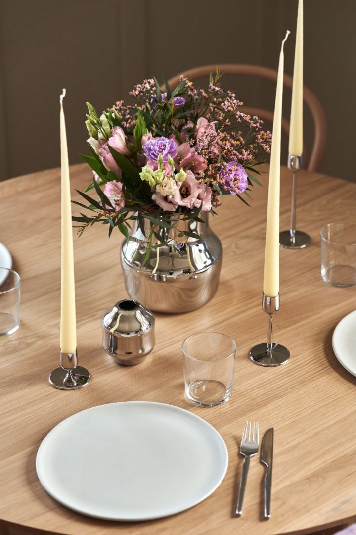 Frühlingserwachen: Eine verspiegelte Edelstahlvase steht in der Mitte eines Tisches mit einem Strauß frischer lilafarbener Blumen.