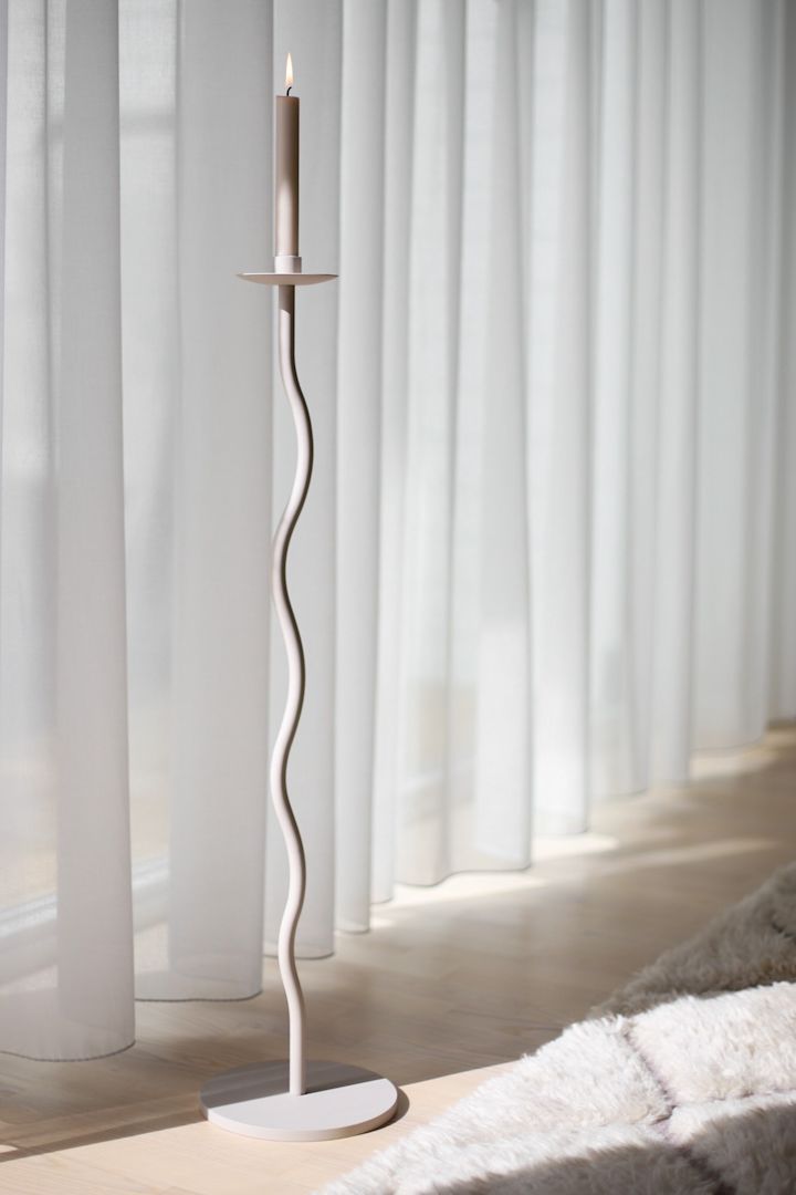 Der große beigefarbene Kerzenhalter Curved von Cooee Design steht in einem Wohnzimmer in Beige vor einem Vorhang.