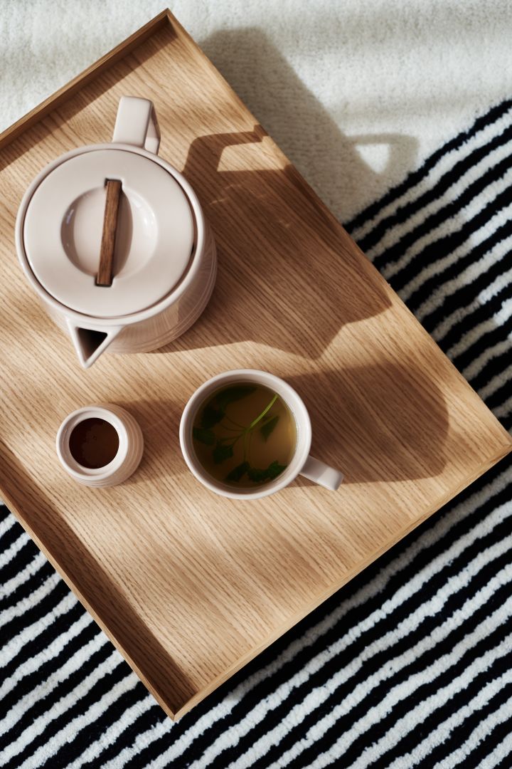 Die beigefarbene Teekanne, Tasse und Zuckerdose der Lines-Serie von NJRD auf einem Holztablett.