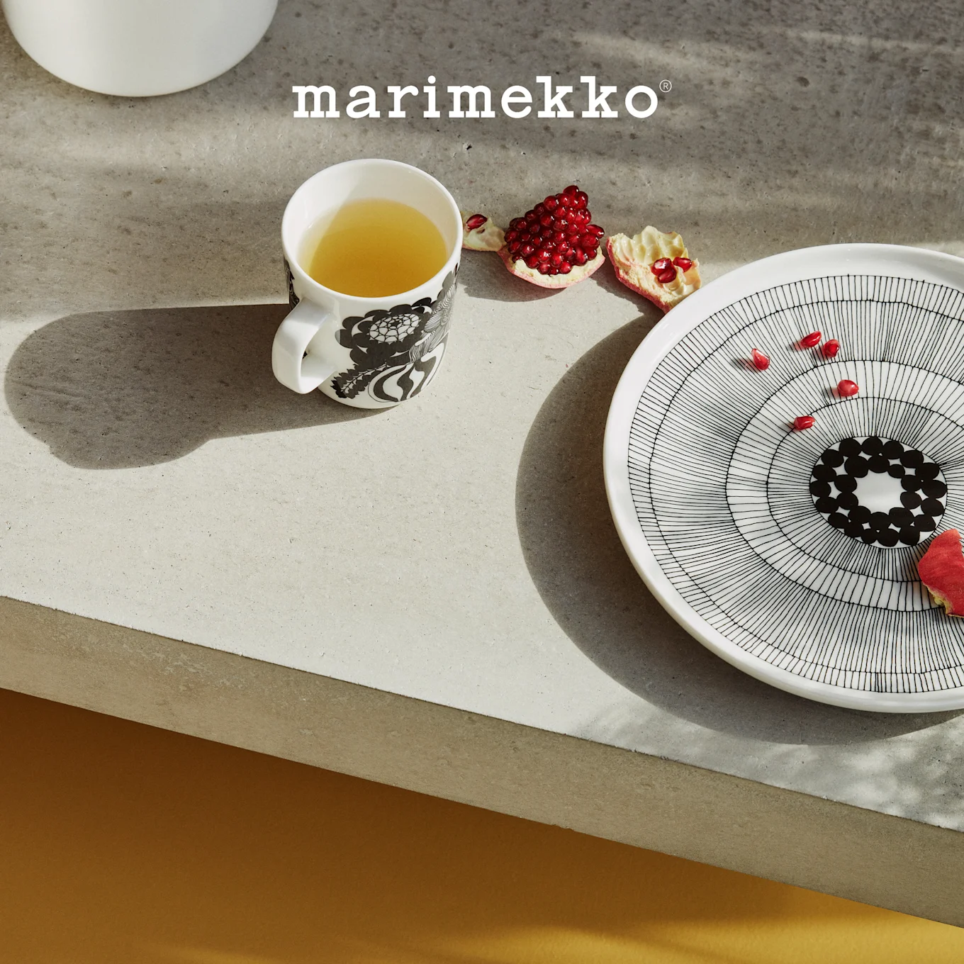 Ein modernes Zimmer mit Marimekko Wohndekor. Auf einem Regal eine grüne Pilzlampe und eine gepunktete Schale mit Obst. Ein gestreifter Stuhl mit einem gepunkteten Kissen und gemusterte Bodenkissen sind zu sehen.