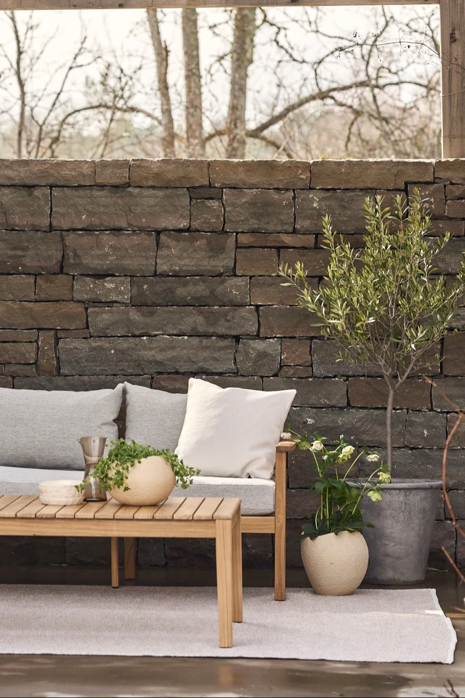 Eine gemütliche Terrasse mit Teppich, einem Sofa und einem Beistelltisch, daneben zahlreiche Pflanzen.