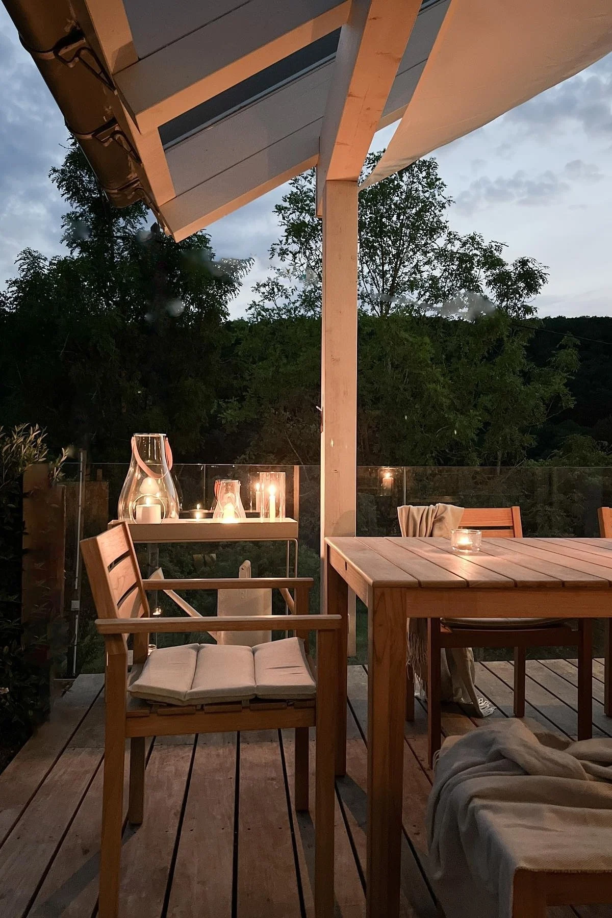 Platzieren Sie mehrere Laternen und Windlichter draußen auf Ihrer Terrasse, um eine gemütliche Atmosphäre zu schaffen. Hier sehen Sie die Design with Light-Laterne von Holmegaard auf dem Terrassentisch aus Holz der deutschen Influencerin @zuhauselig.