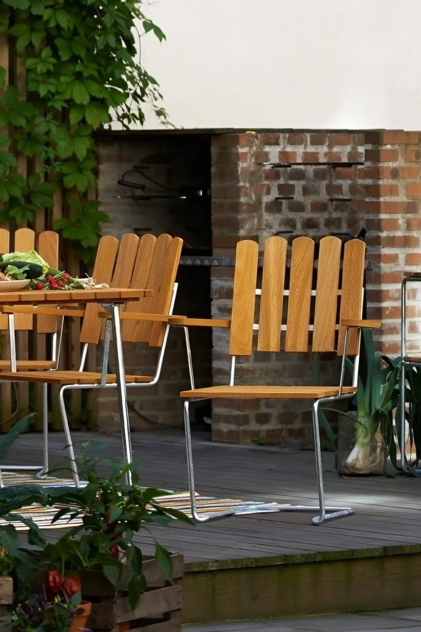 Der A2-Stuhl von Grythyttan besteht aus Teakholz und Stahl, hier auf einer Terrasse zu sehen, und passt somit perfekt in die Gartenmöbel-Trends 2025.