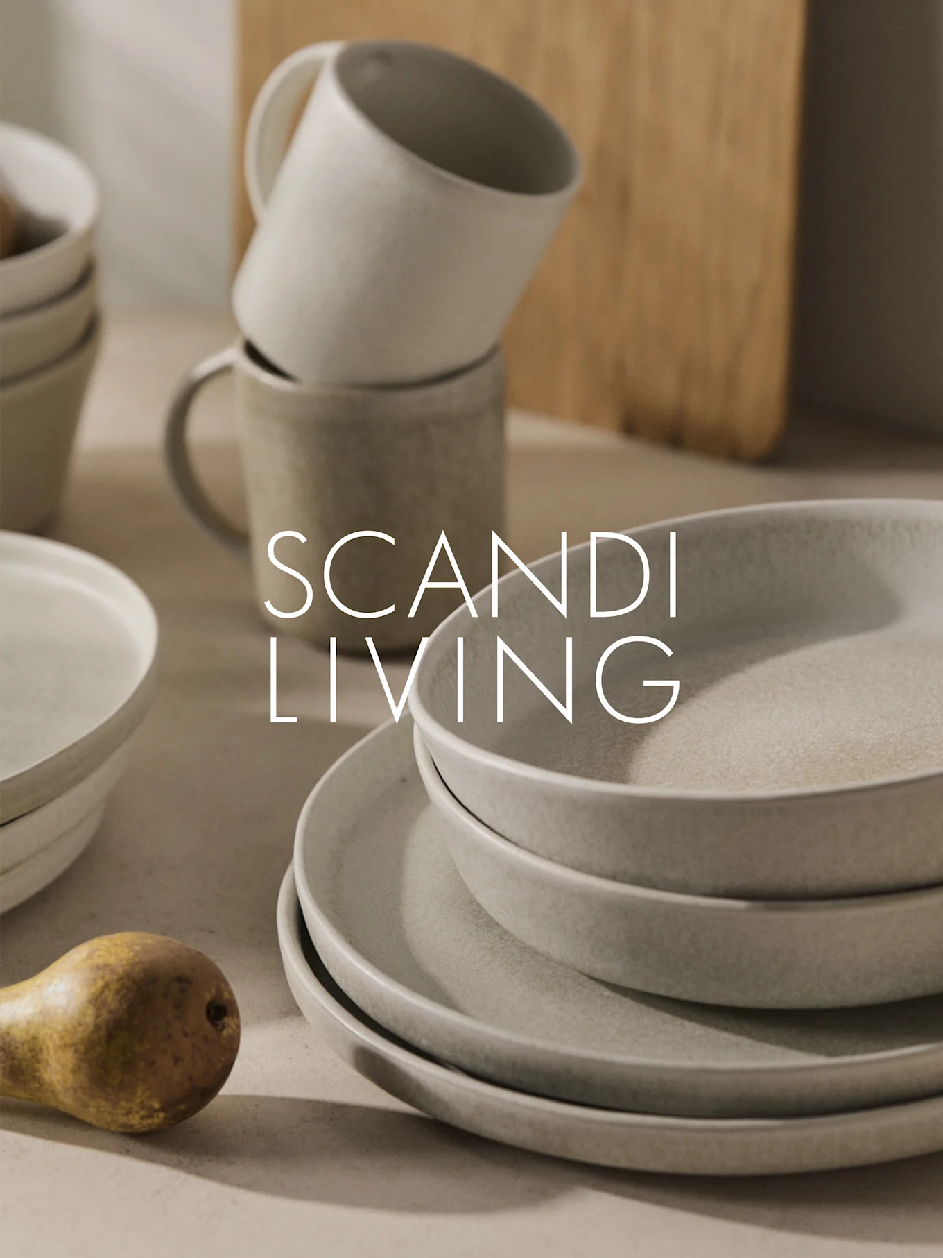 Gestapeltes beiges Keramikgeschirr, Tassen und eine Birne mit "SCANDI LIVING" Schriftzug.