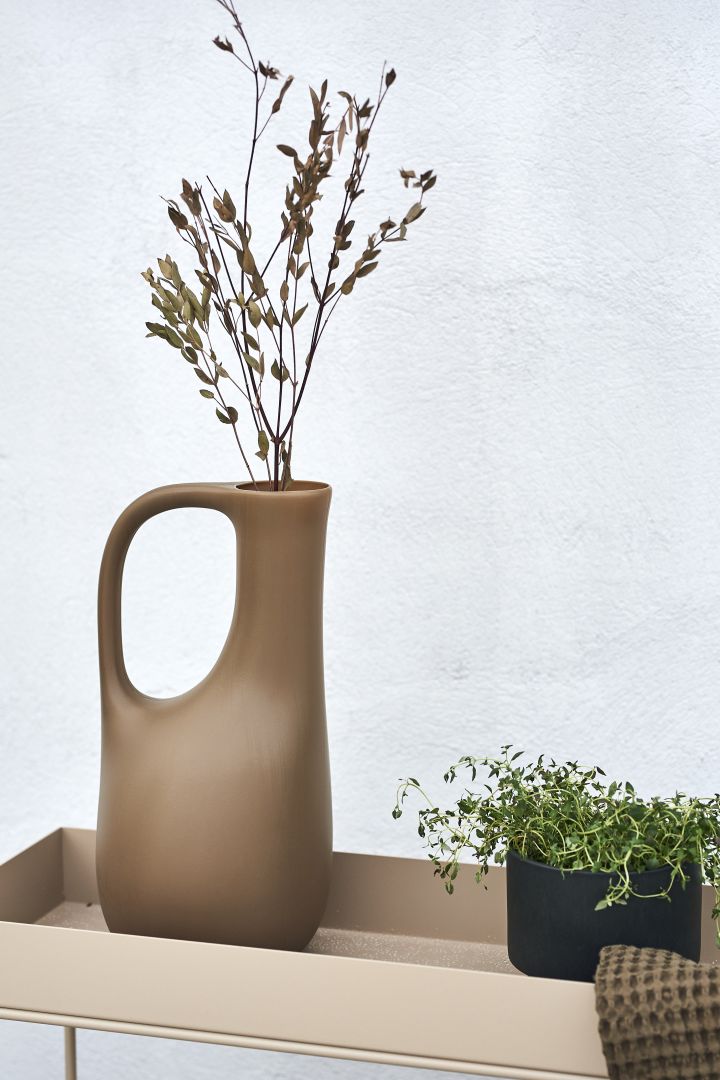 Gestalten Sie Ihren Balkon mit vielen Pflanzen. Nutzen Sie beispielsweise die Wasserkanne von ferm LIVING als Vase und dekorieren Sie sie mit hübschen Gräsern!