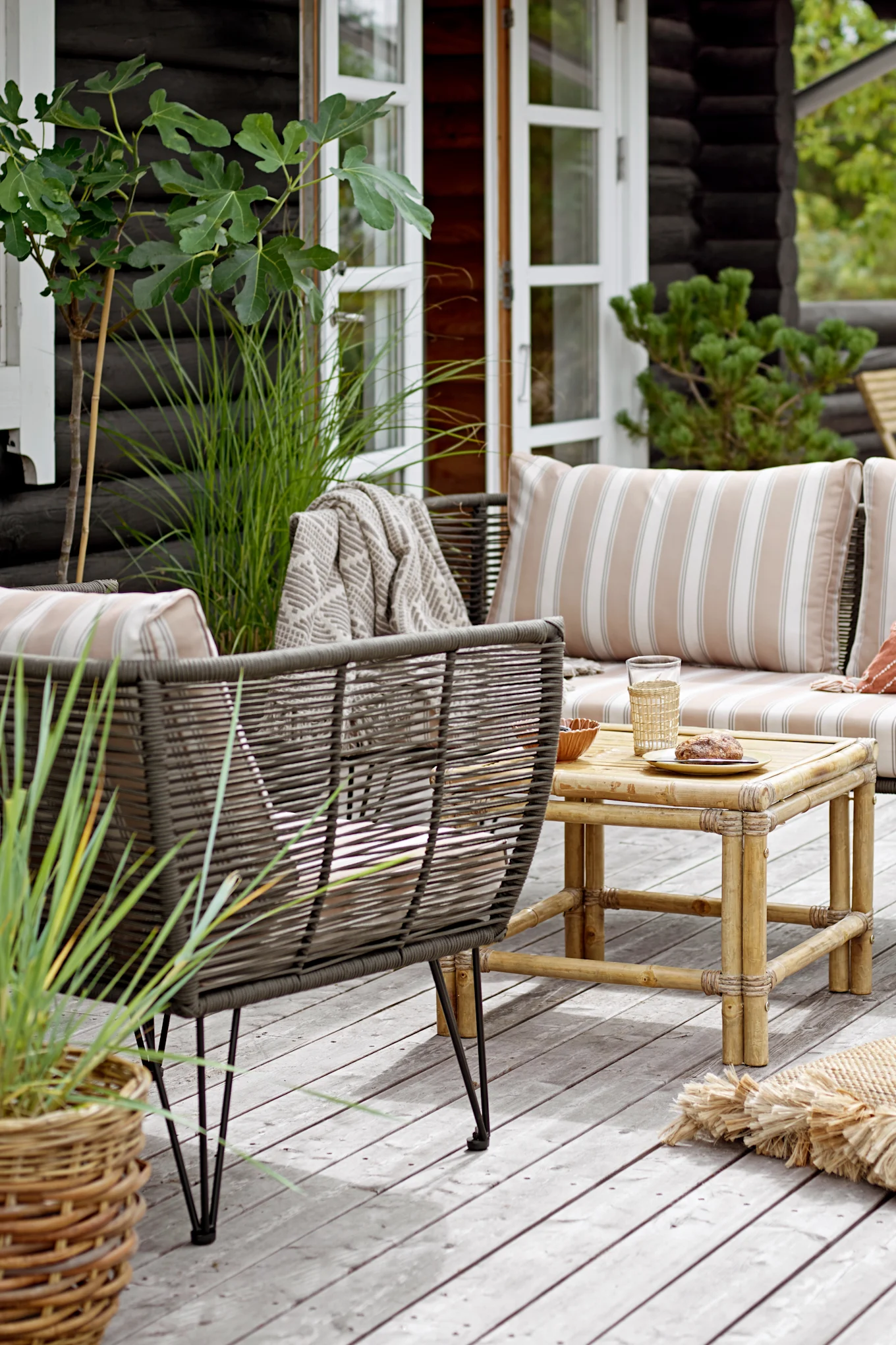 Dekorieren Sie einen Boho-Balkon mit dem Mundo Sofa von Bloomingville, welches zusammen mit dem dazugehörigen Sessel draußen auf einem Balkon steht.