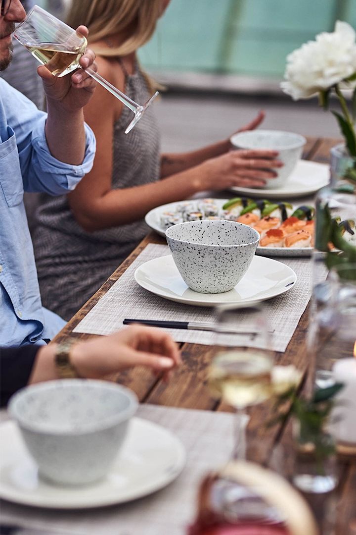 Ein Sommerfest mit weißem Porzellan von der Marke Araba, bei dem die Gesellschaft ein entspanntes Abendessen nach den Grundsätzen der Hygge genießt. 