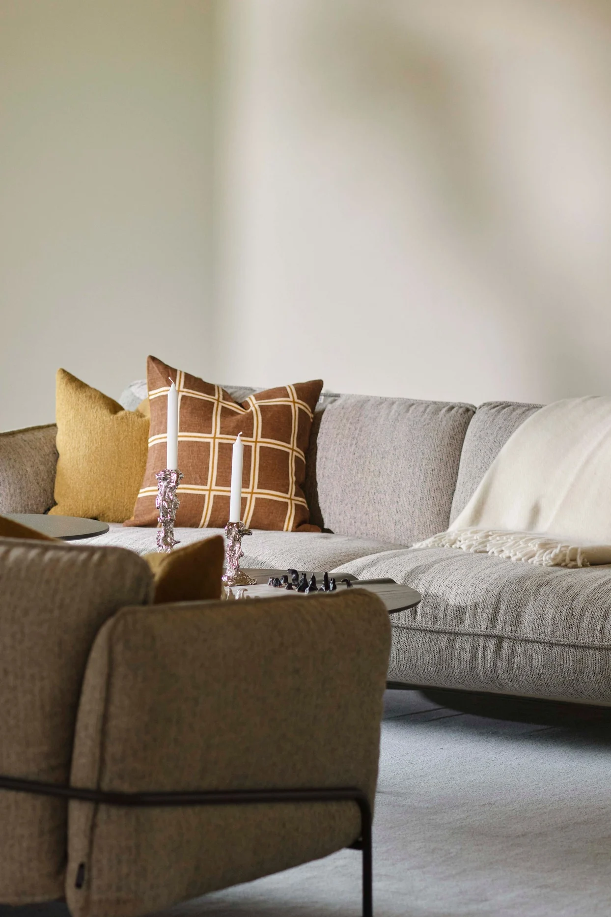 Wohnzimmer mit grauem Ecksofa, gelben und karierten Kissen, weißem Plaid, Couchtisch mit Kerzen und Spielsteinen.